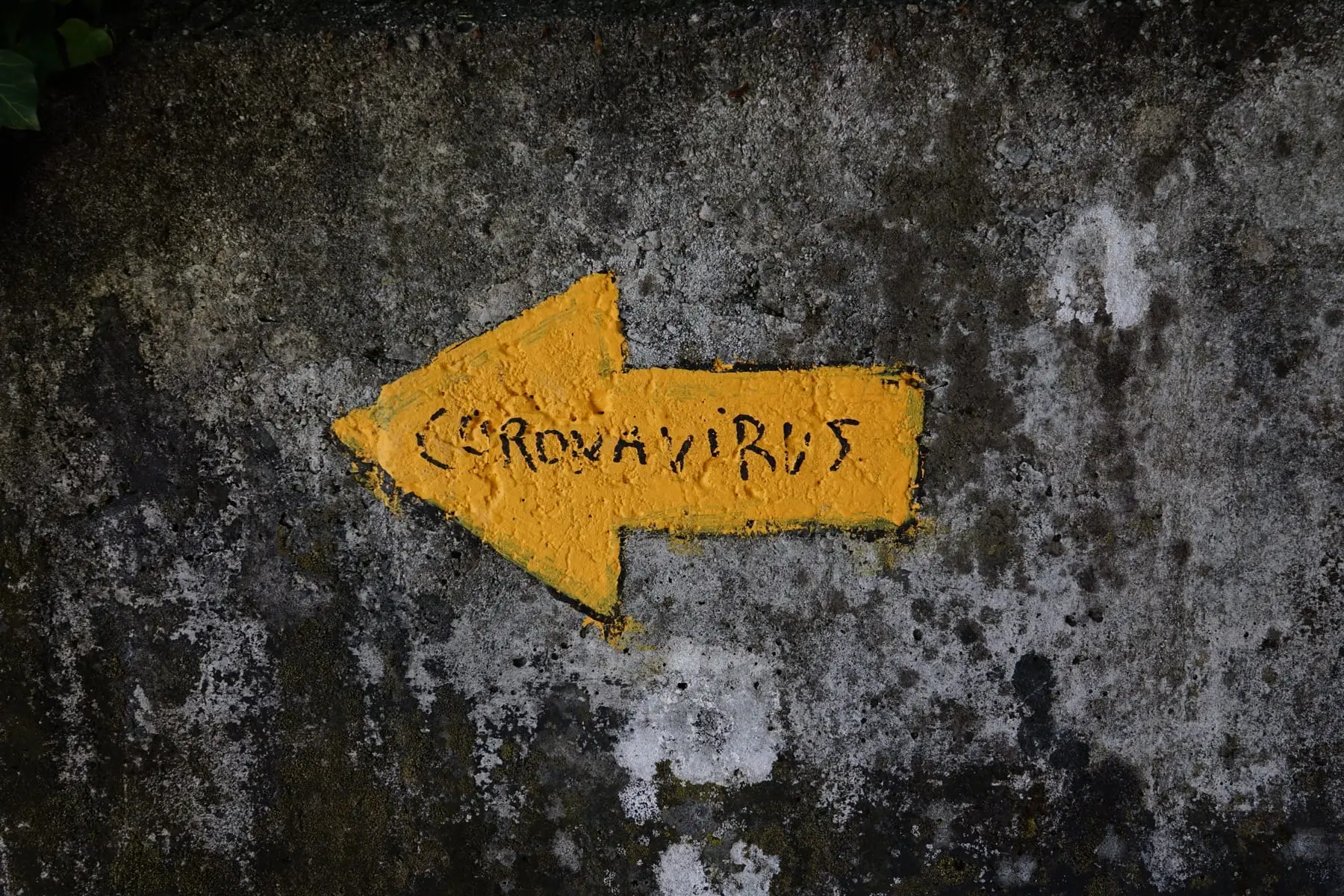 A yellow arrow with coronavirus written inside, painted on an old wall